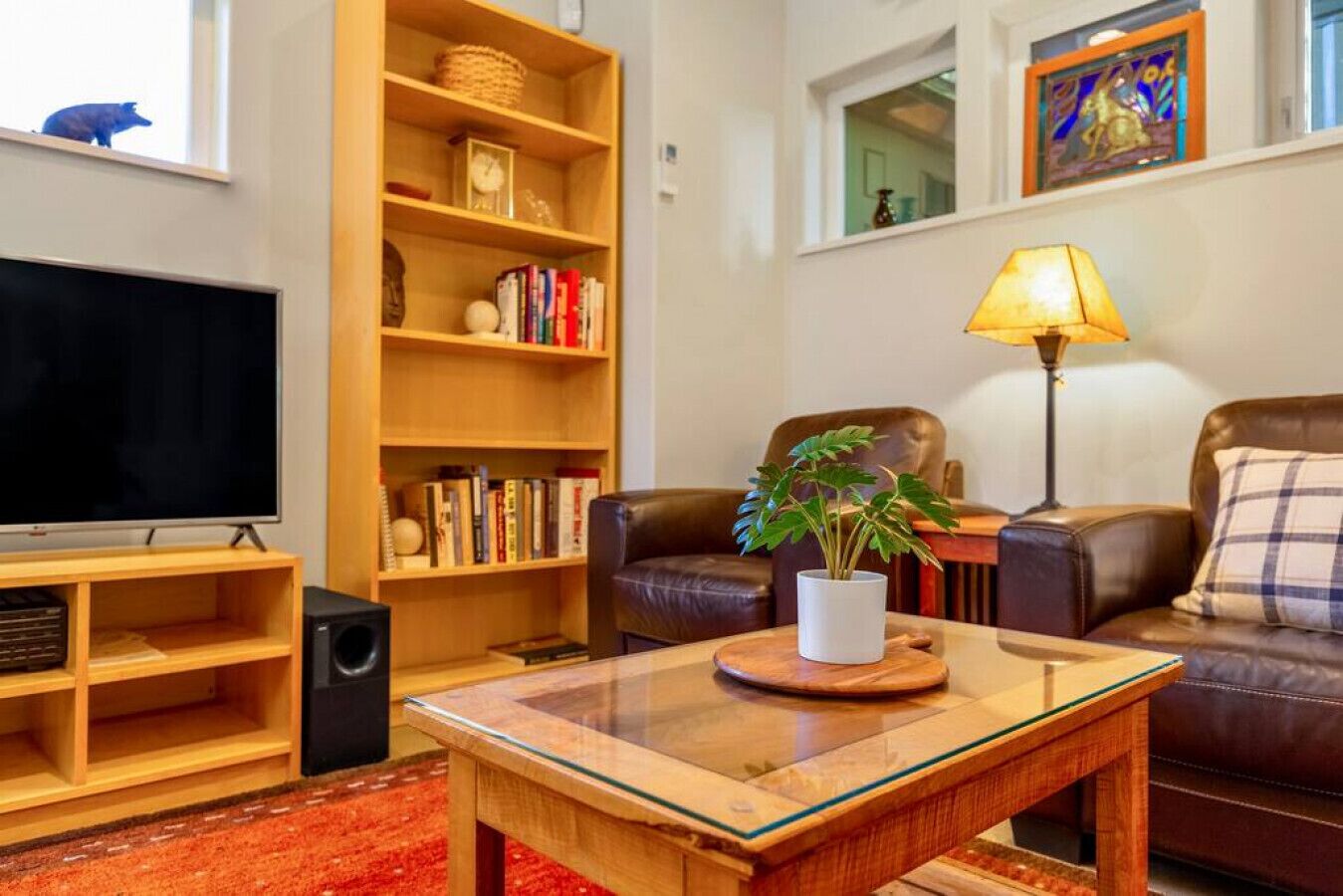 A living room with a television, bookshelves, a coffee table with a plant, a leather sofa, and a lamp.