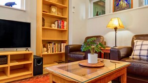 Ein Wohnzimmer mit Fernseher, Bücherregalen, einem Couchtisch mit Pflanze, einer Ledersofa und einer Lampe.