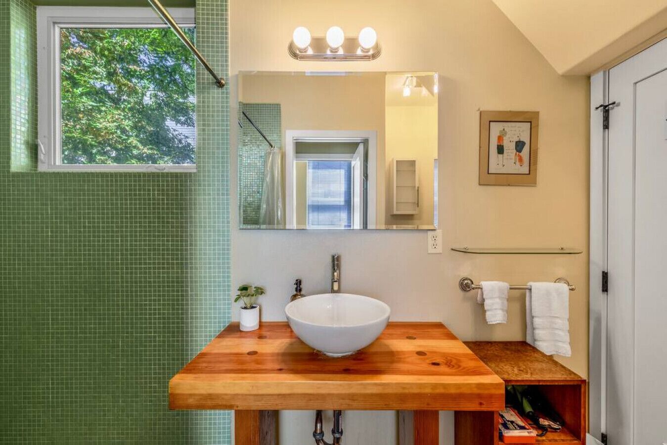 Un baño con tocador de madera, un espejo grande y una ventana con vistas a árboles.