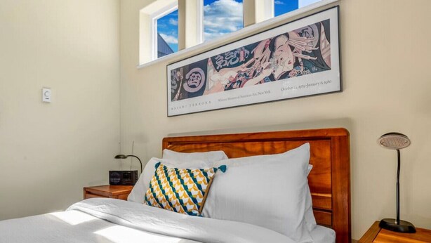 A neatly made bed with white linens and patterned pillows, a wooden headboard, a bedside table with a lamp, and a framed artwork above the bed. - 3214 Seattle · Cozy & Peaceful  2b2.5b South Seattle House  w/AC (Seattle)