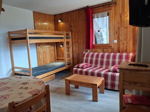 Ein gemütliches Zimmer mit einem Etagenbett, einer Schlafcouch, einem Tisch und einem Fenster mit Vorhängen.