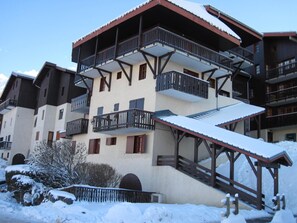 Un immeuble à plusieurs étages, doté de balcons, d’un toit enneigé et d’un escalier en bois menant à l’entrée.