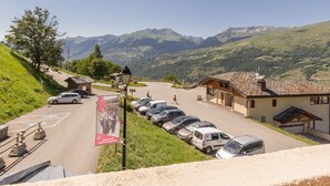 Un estacionamiento con coches, un edificio con tejado de baldosas y montañas al fondo.