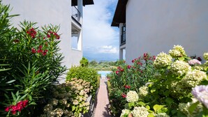 A pathway flanked by lush greenery and flowering plants leading to a pool area. - Appartamento Katy (Polpenazze del Garda)