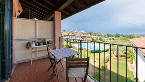 A balcony with a table and chairs, overlooking a swimming pool and a residential area. - Appartamento Katy (Polpenazze del Garda)