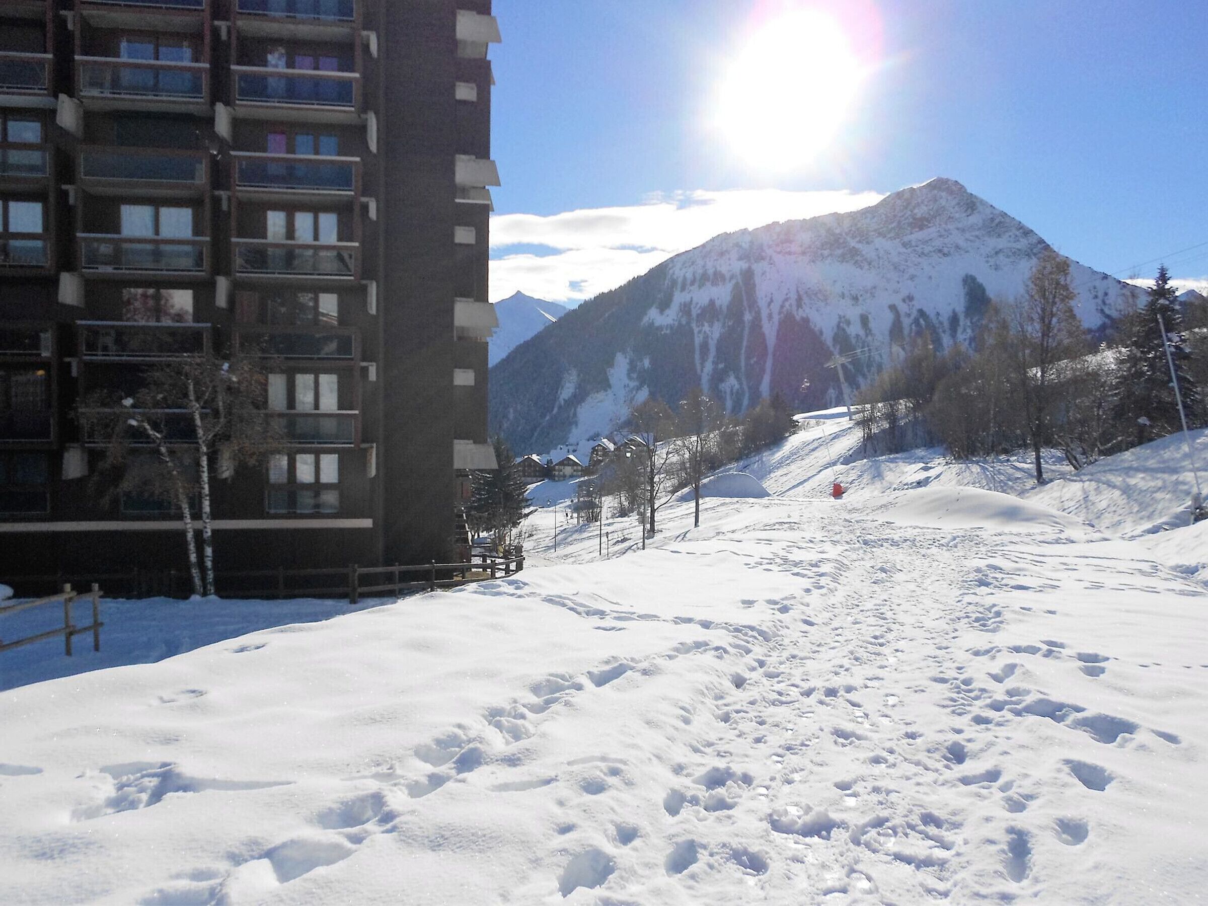A snow-covered ski slope with a mountain in the background and a building with multiple balconies.