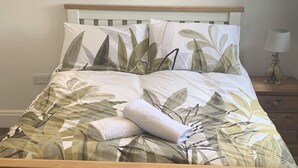 Una cama con colcha y almohadas estampadas, un cabecero de madera, una mesita de noche con lámpara y un enchufe.