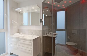 Un baño moderno con cabina de ducha de vidrio, tocador doble con un espejo grande y un inodoro.