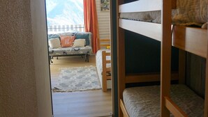 A room with bunk beds, a sofa with cushions, a patterned rug, and a view of mountains through a window with orange curtains. - Studio cabin 27 sqm, 4 people, pets allowed, balcony (Orcières Merlette)