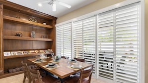 A dining area with a wooden table set for four, surrounded by chairs. There is a built-in shelf with decorative items and books. - It's A Mirage - Victoria Falls Home (Rancho Mirage)