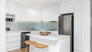 Una cucina moderna con mobili bianchi, un frigorifero in acciaio inossidabile, un forno integrato e una ciotola di legno sul piano cucina.
