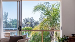 Una stanza con un'ampia porta scorrevole in vetro che dà su un balcone con palme e vista sul paesaggio circostante.
