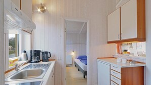 A compact kitchen with a sink, coffee maker, and cabinets. A bed is visible in the adjacent room. - Schmugglerstieg 1 - Dorf 6 (Lübeck)