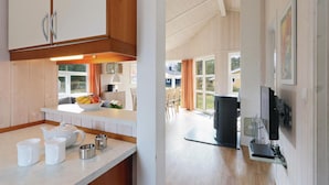 A modern kitchen with wooden cabinets, a countertop with a bowl of fruit, and a dining area with a table and chairs. - Frische Brise 3 - Dorf 2 (Lübeck)
