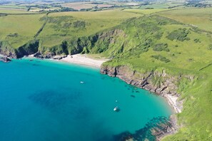 An aerial view of a coastal area with a beach, cliffs, and clear turquoise waters.