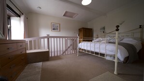 Un dormitorio con estructura de cama de metal blanco, cómoda de madera, piso alfombrado y una ventana con cortinas.