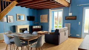A room with a wooden dining table, chairs, a sofa, a fireplace, and a television. - L'hippocampe - Appt Mezzanine Centre D'arromanches (Arromanches-les-Bains)