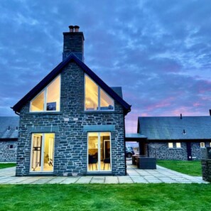 Une maison en pierre avec un toit à pignon, de grandes fenêtres et une pelouse bien entretenue.