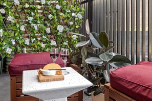Une terrasse avec une table dressée pour un repas, comprenant du fromage, des crackers et des verres à vin.