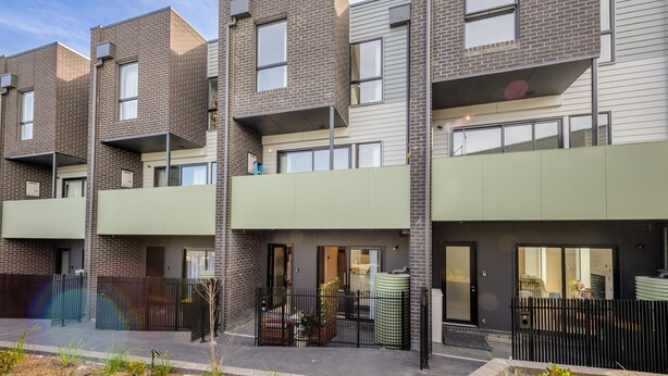 Um edifício moderno de apartamentos, com várias unidades, varandas e portão fechado.