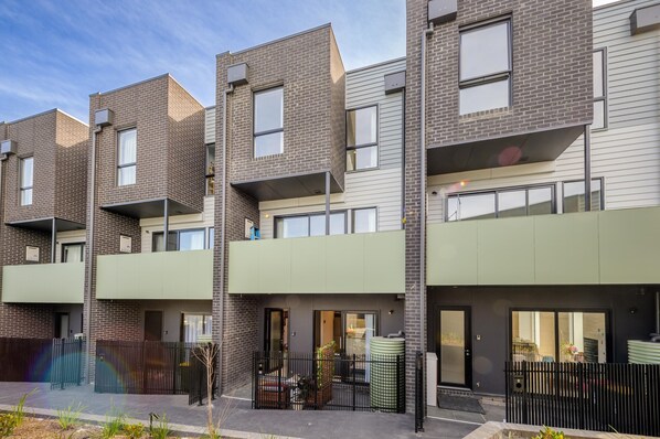 A modern apartment building with multiple units, balconies, and a gated entrance.