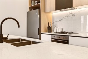 A modern kitchen with a stainless steel refrigerator, a curved faucet, and a marble backsplash. - StayCentral - Boulevard Gardens (Coburg) - Sacramento Way, Coburg - 3 Bedrooms, 4 Beds, 2 Bathrooms, 2 secure undercover parking spots. (Coburg)