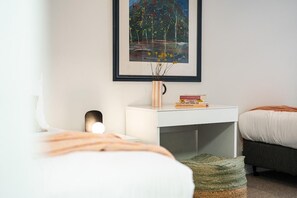 A bedroom with a bed, bedside table, lamp, framed artwork, and a small bookshelf.