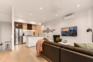 A modern living space with a kitchen, a sofa, a cityscape painting, and a ceiling fan.
