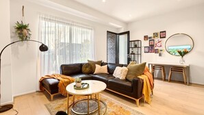 Uma sala de estar moderna com um sofá de couro preto, uma mesa de centro redonda e uma janela grande com cortinas leves.
