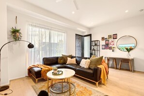 A modern living room with a black leather sofa, a round coffee table, and a large window with sheer curtains.