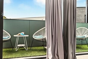 A balcony with two white wicker chairs, a small round table, and a pair of shoes on the table. - StayCentral - Boulevard Gardens (Coburg) - Sacramento Way, Coburg - 3 Bedrooms, 4 Beds, 2 Bathrooms, 2 secure undercover parking spots. (Coburg)