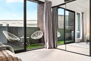 A modern balcony with glass doors, white wicker chairs, and a small table.
