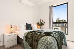 A bedroom with a bed, bedside table, lamp, and a window with a view.
