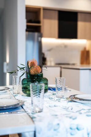 A dining table with a green vase, two clear glasses, and a floral arrangement. - StayCentral - Boulevard Gardens (Coburg) - Sacramento Way, Coburg - 3 Bedrooms, 4 Beds, 2 Bathrooms, 2 secure undercover parking spots. (Coburg)