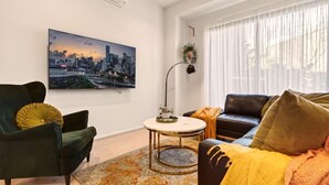 Sala moderna com pintura de paisagem urbana, mesa de centro redonda e sofá com manta.