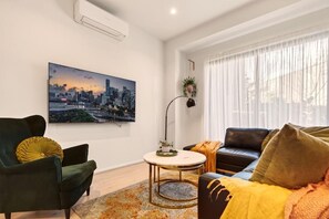 A modern living room with a cityscape painting, a round coffee table, and a sofa with a throw blanket.