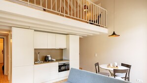 A compact living space with a kitchenette, a dining area with a round table and chairs, a sofa, and a balcony with a railing. - Brilliant Duplex Studio w/ Balcony for 3 in Center (Oporto)