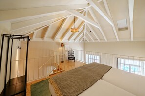 A high-ceilinged room with a sloped roof, a staircase, a bed, and a chair.