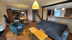 Un salon avec un canapé, une table en bois et un fauteuil bleu. Un escalier mène à un autre niveau.