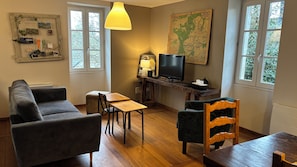 Un salon meublé comprenant un canapé, une table, une chaise, un téléviseur, une lampe et une carte accrochée au mur.