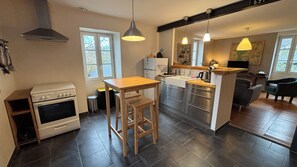 A modern kitchen with a stove, sink, and bar area, featuring dark flooring and pendant lighting.
