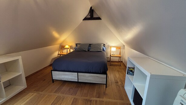 Una camera da letto con un letto, due lampade da comodino, un pavimento in legno e una scaffalatura bianca.