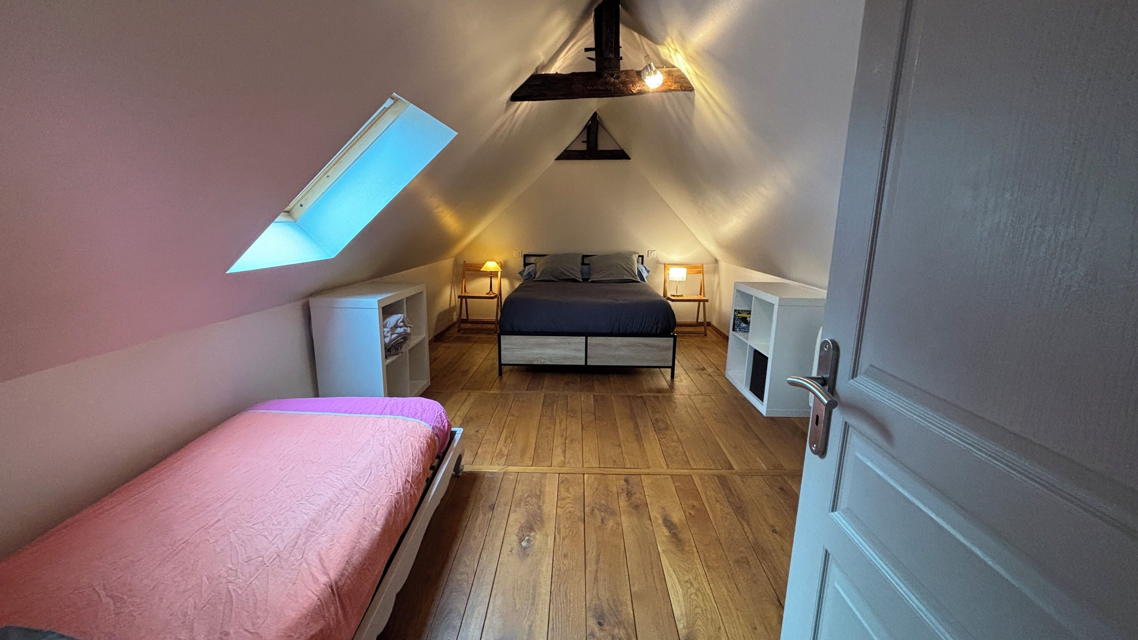 A bedroom with a sloped ceiling, a bed, bedside tables, a wardrobe, and a skylight.