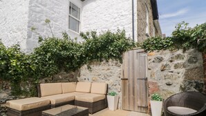 Une terrasse avec un canapé d’angle, deux tables basses en osier et un fauteuil en osier.