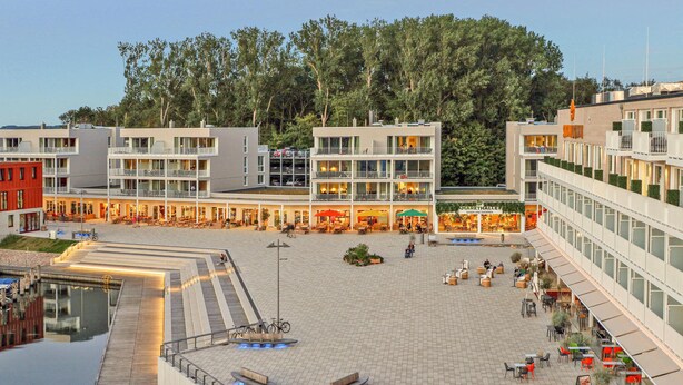 A modern building with multiple floors, outdoor seating areas, and a central open space. - Dünenvilla Comfort (Lübeck)