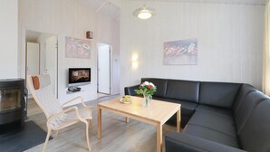 Ett vardagsrum med en svart lädersoffa, ett soffbord i trä, en tv som är monterad på väggen och en öppen spis.