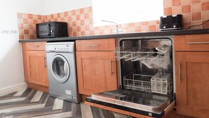 A compact kitchen with a washing machine, dishwasher, and a microwave on the countertop. - Beautiful 2-bed Apartment in Poulton-le-fylde (Poulton-le-Fylde)
