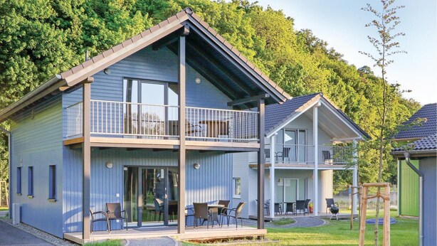 Une maison à deux étages avec un balcon, de grandes fenêtres et une cour gazonnée.