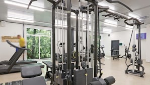 A gym with various exercise equipment, a treadmill, and a large window with a view of trees. - Ferienhausdorf Thale (Thale)