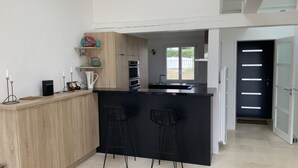 A modern kitchen with a black island, two bar stools, a wooden cabinet, and a window with a view. - Rare! Seafront vacation home with direct access to sea and beach (Pornic)